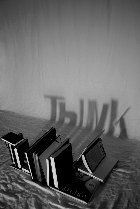 Thibodeau Photography «Think» Se ven unos libros en el suelo colocados de tal forma que en la pared se ve la sombra de la palabra think
